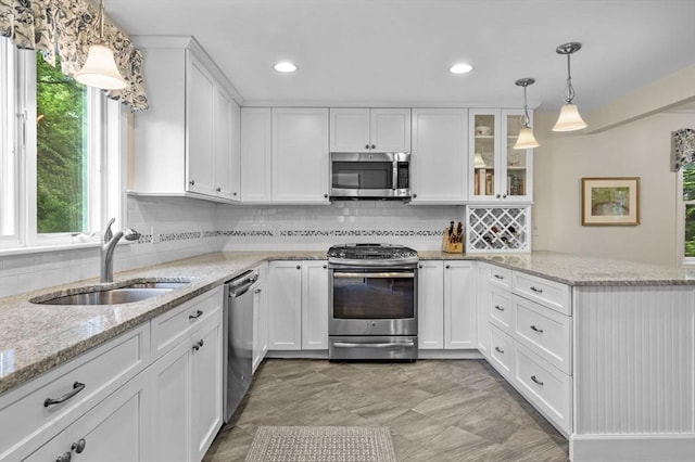 kitchen with decorative light fixtures, appliances with stainless steel finishes, glass insert cabinets, white cabinets, and a sink