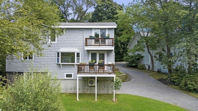 rear view of property with a yard, a balcony, and driveway