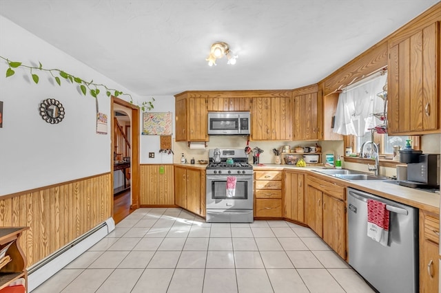 kitchen with sink, stainless steel appliances, a baseboard heating unit, wooden walls, and light tile patterned floors