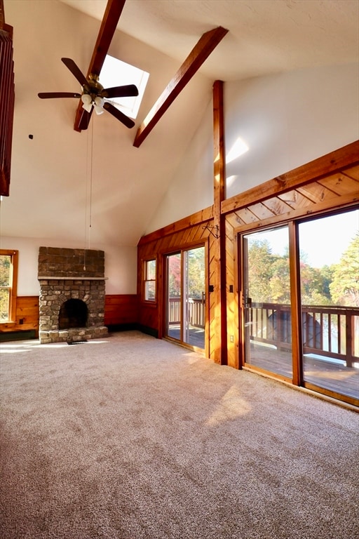 unfurnished living room featuring beam ceiling, wooden walls, carpet, high vaulted ceiling, and a skylight