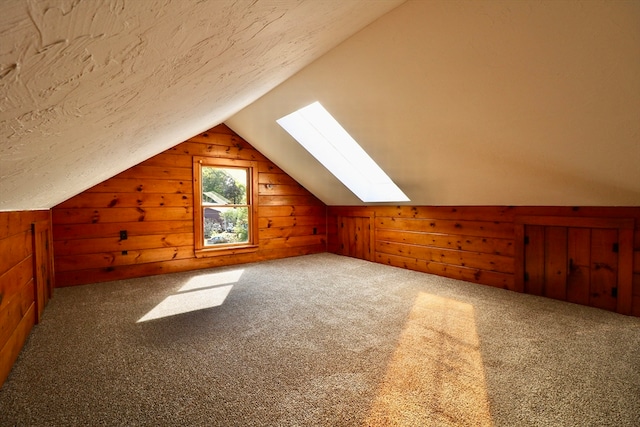 additional living space with carpet flooring, vaulted ceiling with skylight, and wooden walls