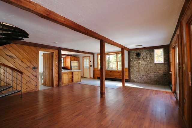 unfurnished living room with beam ceiling, wood walls, and light hardwood / wood-style flooring