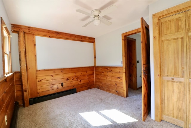 spare room featuring light carpet, baseboard heating, wooden walls, and ceiling fan