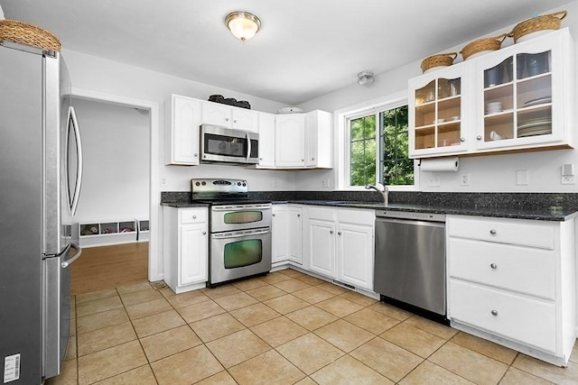 kitchen with appliances with stainless steel finishes, white cabinets, glass insert cabinets, and light tile patterned floors