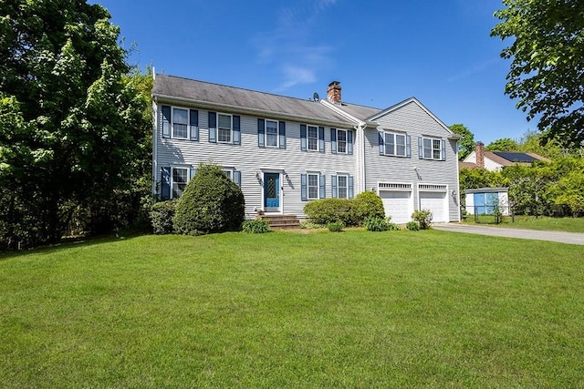colonial-style house featuring a chimney, concrete driveway, an attached garage, and a front yard