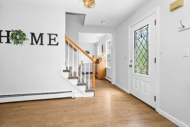 foyer entrance featuring wood finished floors, a baseboard heating unit, and stairway