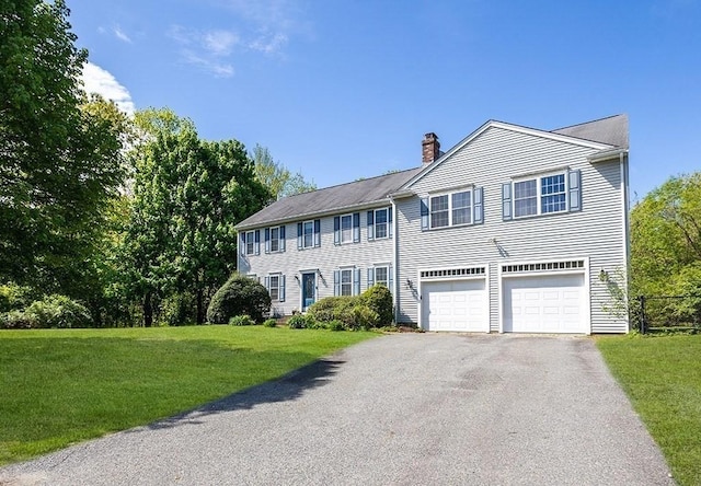 colonial inspired home with a chimney, driveway, an attached garage, and a front lawn