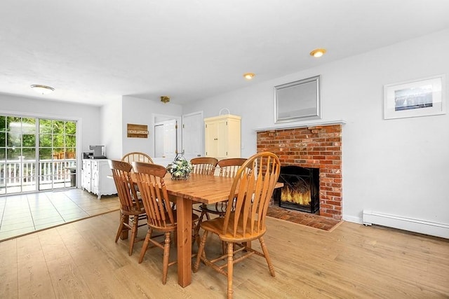 dining area featuring light wood-type flooring, a brick fireplace, and a baseboard heating unit