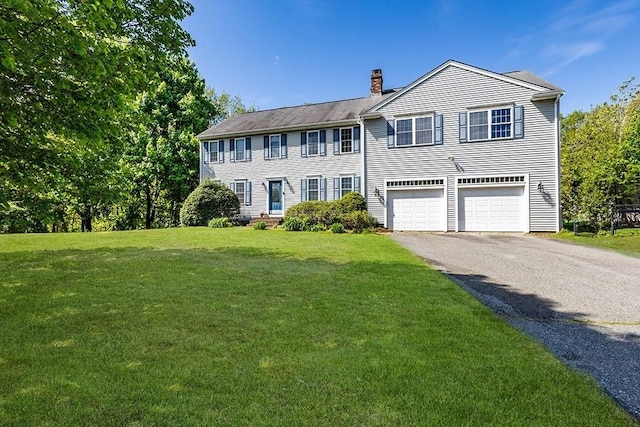 colonial home featuring a chimney, asphalt driveway, a garage, and a front lawn