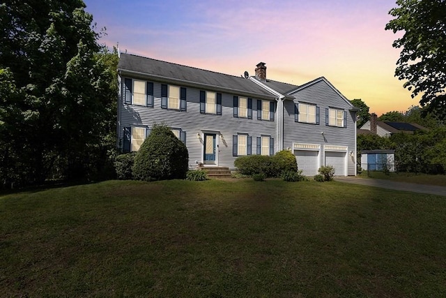 colonial inspired home featuring a chimney, concrete driveway, a front lawn, and an attached garage