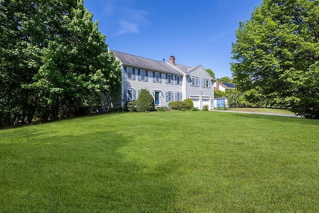 back of house with a chimney, an attached garage, and a yard