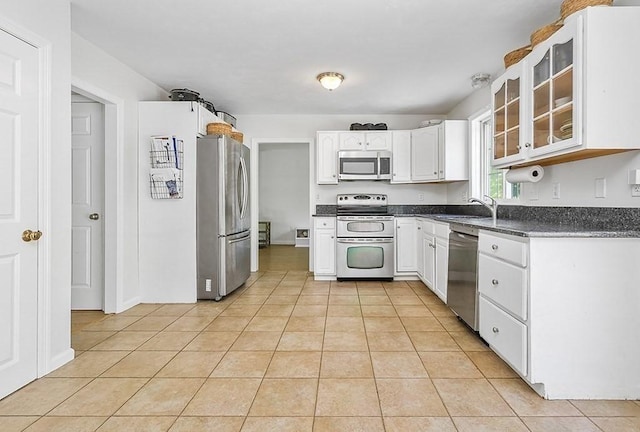 kitchen featuring stainless steel appliances, light tile patterned floors, dark countertops, and glass insert cabinets