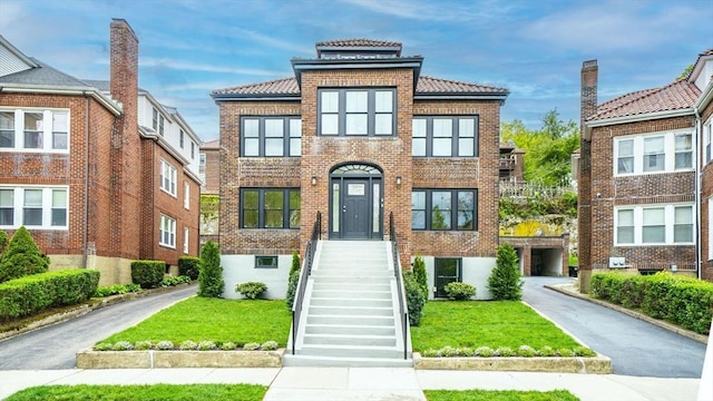 view of front of house with a tiled roof, brick siding, and a front yard