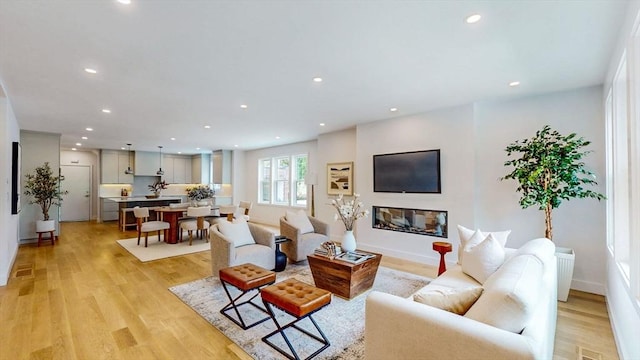 living room featuring recessed lighting, light wood-style flooring, baseboards, and a glass covered fireplace