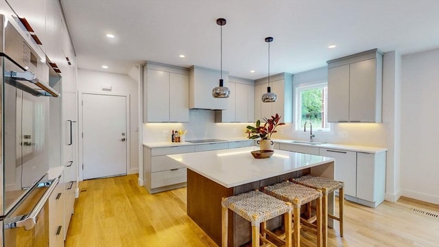 kitchen featuring a sink, light wood-type flooring, black electric stovetop, a kitchen island, and recessed lighting
