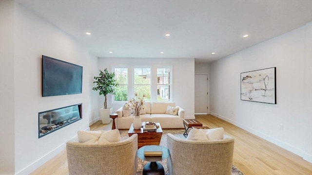 living room featuring light wood-style flooring, recessed lighting, baseboards, and a glass covered fireplace