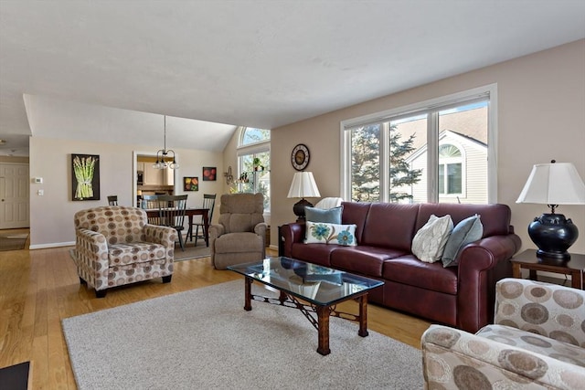 living room with vaulted ceiling, an inviting chandelier, and light wood-type flooring