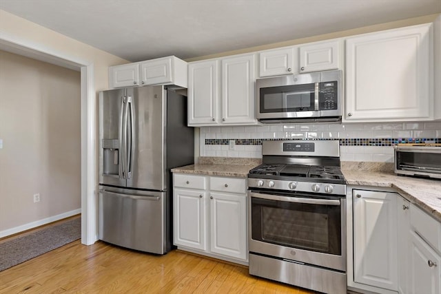 kitchen with appliances with stainless steel finishes, white cabinets, and tasteful backsplash