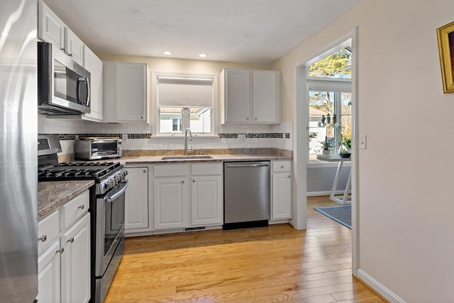 kitchen with backsplash, light hardwood / wood-style floors, sink, white cabinetry, and stainless steel appliances