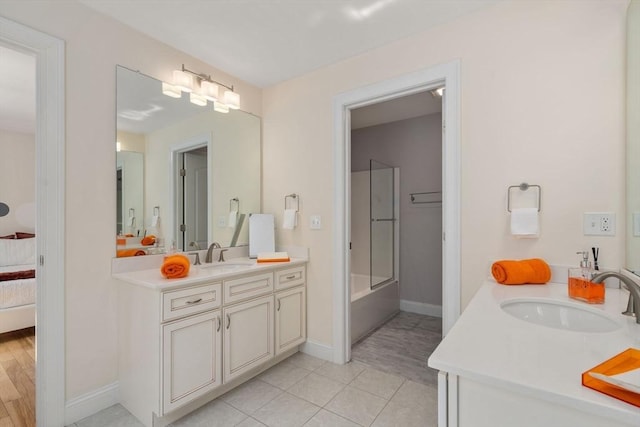 ensuite bathroom featuring two vanities, baseboards, tile patterned floors, and tub / shower combination