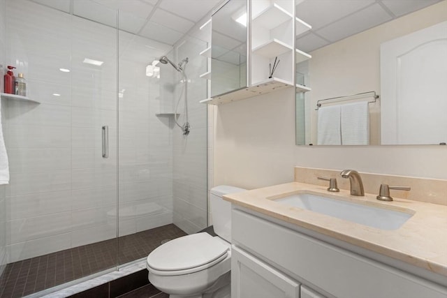 bathroom featuring toilet, a stall shower, a paneled ceiling, and vanity