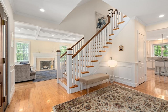 stairs with hardwood / wood-style floors, beamed ceiling, coffered ceiling, recessed lighting, and a fireplace