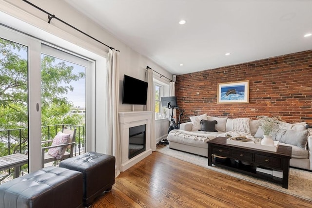 living room with recessed lighting, wood finished floors, a glass covered fireplace, and brick wall