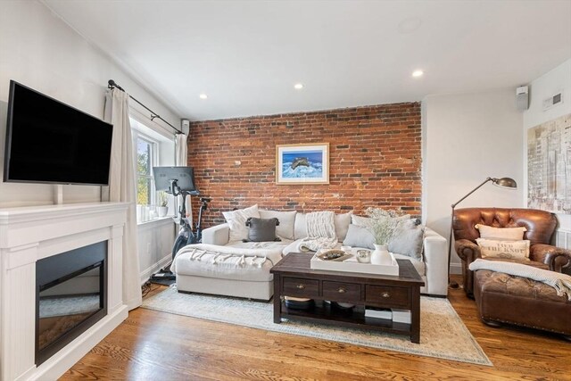 living area with baseboards, an accent wall, brick wall, a glass covered fireplace, and wood finished floors