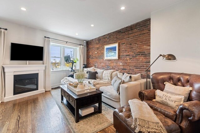 living area featuring recessed lighting, a glass covered fireplace, brick wall, and wood finished floors