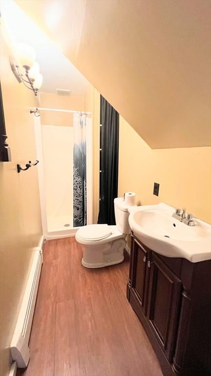 628 Malden St, Revere, MA 02151 - full bathroom with a baseboard heating unit, wood finished floors, toilet, a stall shower, and vanity