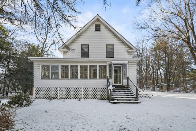 snow covered rear of property featuring a sunroom