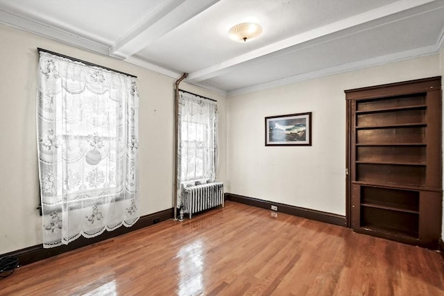 spare room featuring beam ceiling, radiator, crown molding, and wood-type flooring