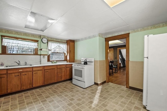 kitchen with white appliances, a drop ceiling, tile walls, and sink