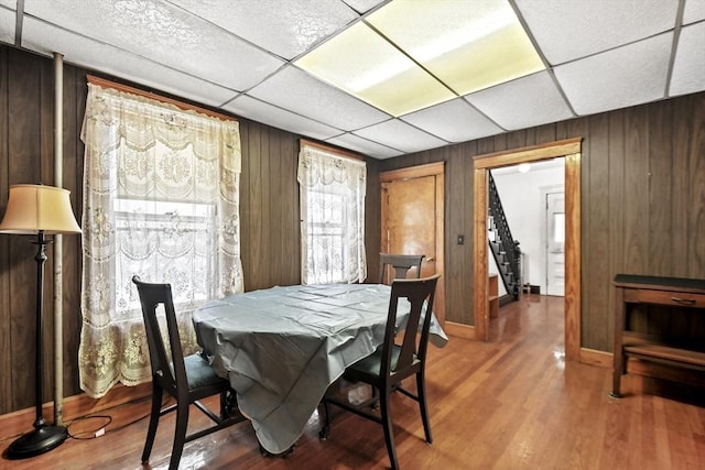 dining area featuring hardwood / wood-style flooring, a paneled ceiling, and wooden walls