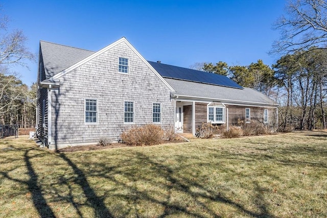 view of front of home featuring a front lawn, solar panels, and roof with shingles