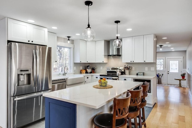 kitchen with appliances with stainless steel finishes, white cabinetry, a kitchen island, and wall chimney range hood