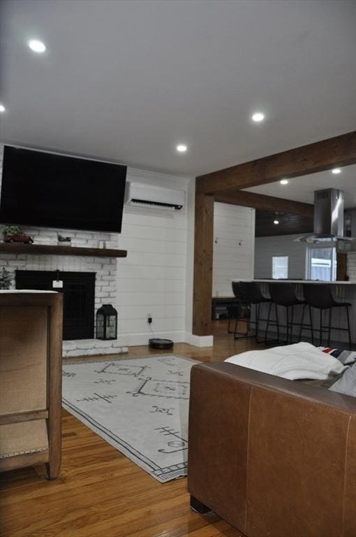 living room featuring a wall mounted air conditioner, beamed ceiling, hardwood / wood-style floors, and a brick fireplace