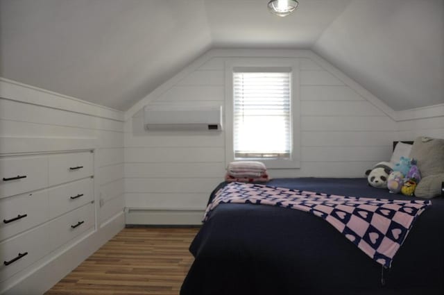 bedroom featuring lofted ceiling, hardwood / wood-style floors, a wall unit AC, and a baseboard heating unit