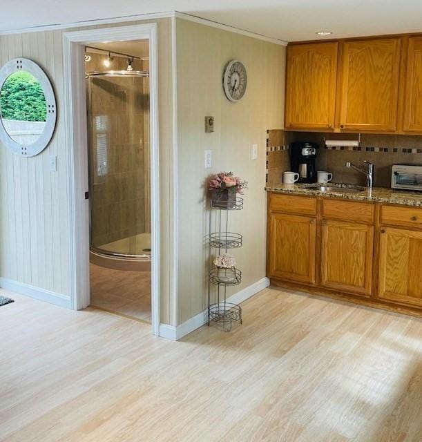 kitchen with sink, ornamental molding, light wood-type flooring, light stone countertops, and tasteful backsplash