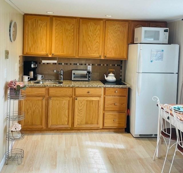 kitchen featuring light wood-type flooring, tasteful backsplash, light stone counters, white appliances, and sink