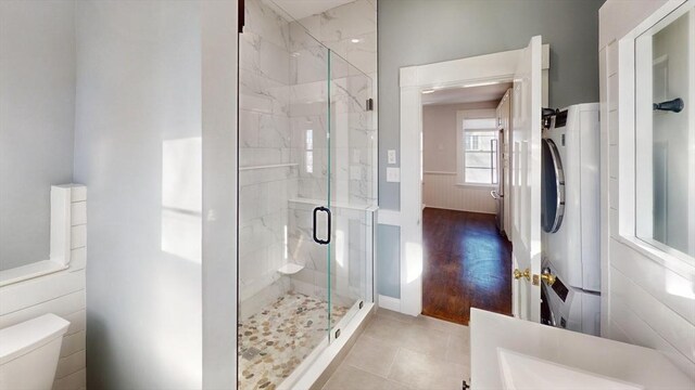 bathroom with tile patterned floors, stacked washing maching and dryer, an enclosed shower, and toilet