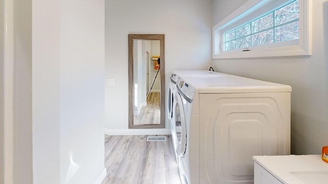 clothes washing area with separate washer and dryer and light wood-type flooring