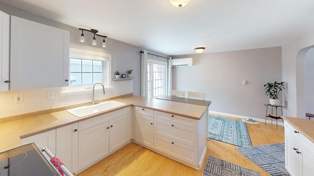 kitchen featuring sink, light hardwood / wood-style flooring, white cabinetry, a wall unit AC, and kitchen peninsula