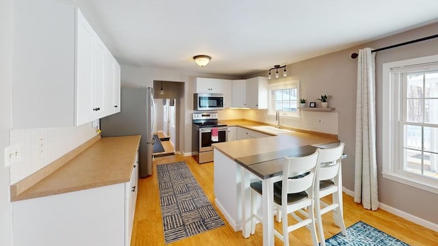 kitchen with appliances with stainless steel finishes, white cabinetry, sink, kitchen peninsula, and light hardwood / wood-style flooring