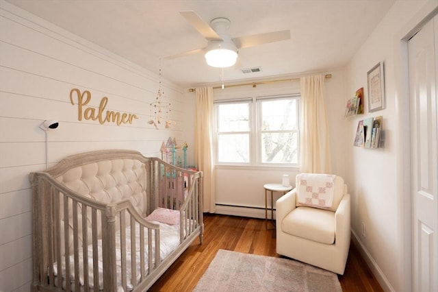 bedroom with baseboard heating, a ceiling fan, wood finished floors, and visible vents