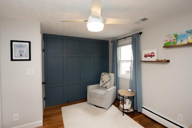 sitting room featuring visible vents, wood finished floors, baseboards, baseboard heating, and a ceiling fan