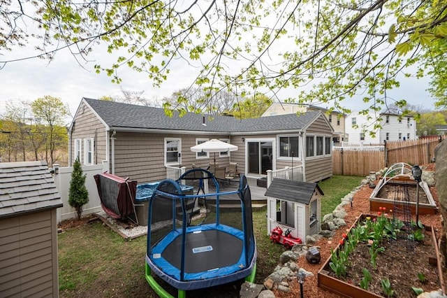 back of property with a fenced backyard, a vegetable garden, a sunroom, a lawn, and a trampoline