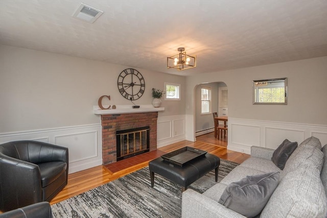 living area with visible vents, wainscoting, wood finished floors, baseboard heating, and arched walkways