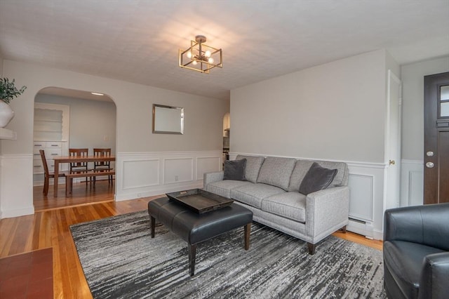 living area featuring arched walkways, a baseboard radiator, a wainscoted wall, and wood finished floors