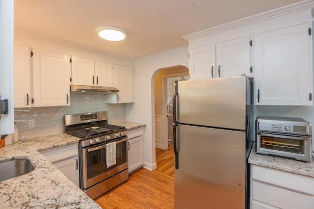kitchen featuring light wood finished floors, stainless steel appliances, white cabinetry, tasteful backsplash, and under cabinet range hood